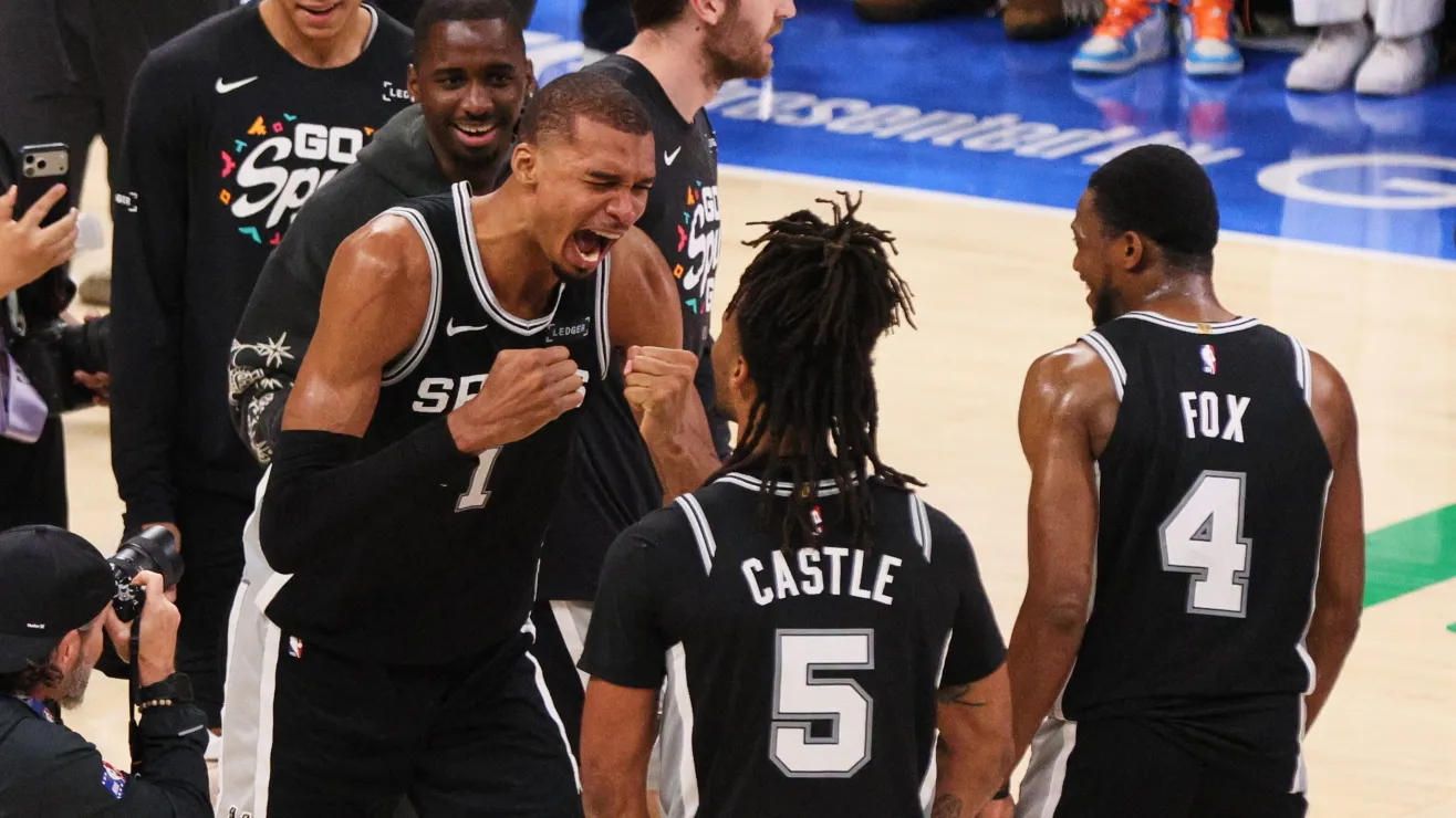 A basketball player wearing number 1 shouts and fists pump while two teammates, Castle #5 and Fox #4, look on in celebration on the court.