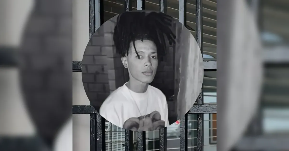 Circular portrait of a young person with short dreadlocks wearing a white shirt, against a brick wall.