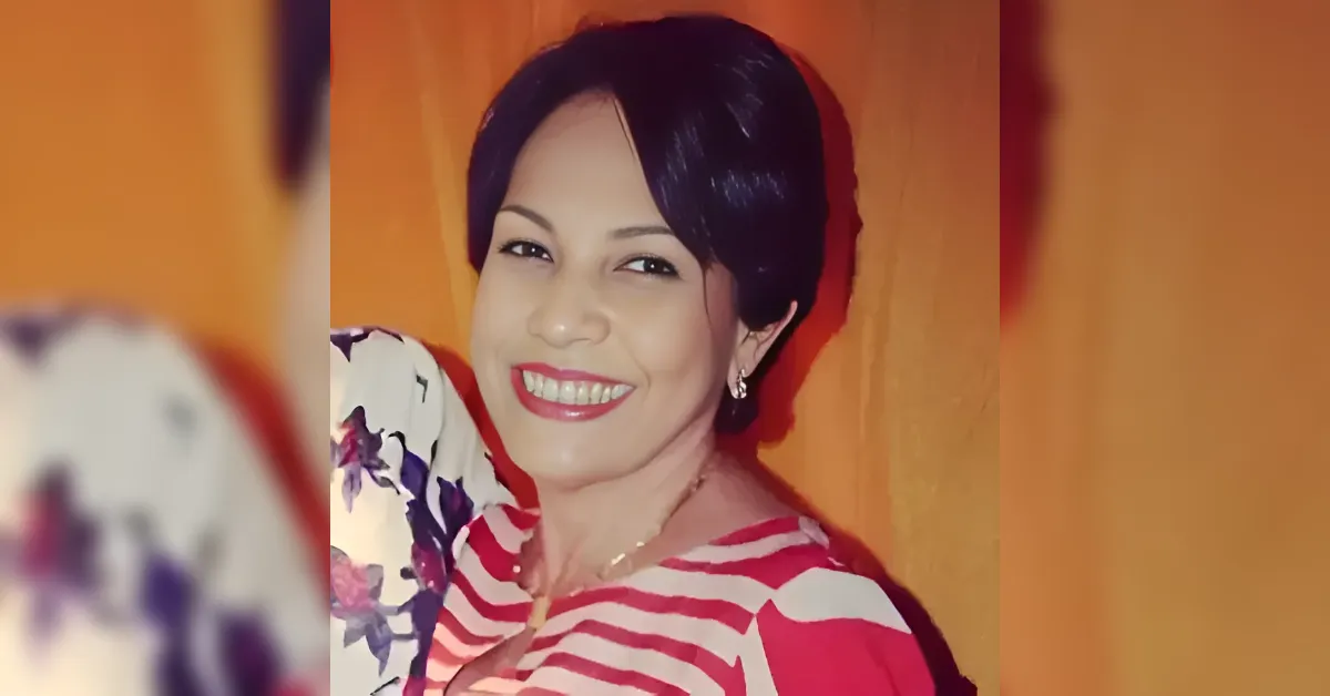 Smiling woman with short black hair wearing a red-and-white striped top, gold necklace, and earrings against an orange background.