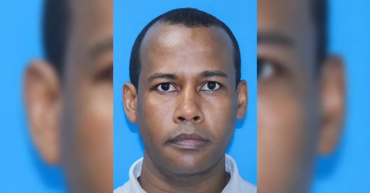 Close-up portrait of a man with short hair against a blue background, neutral expression.