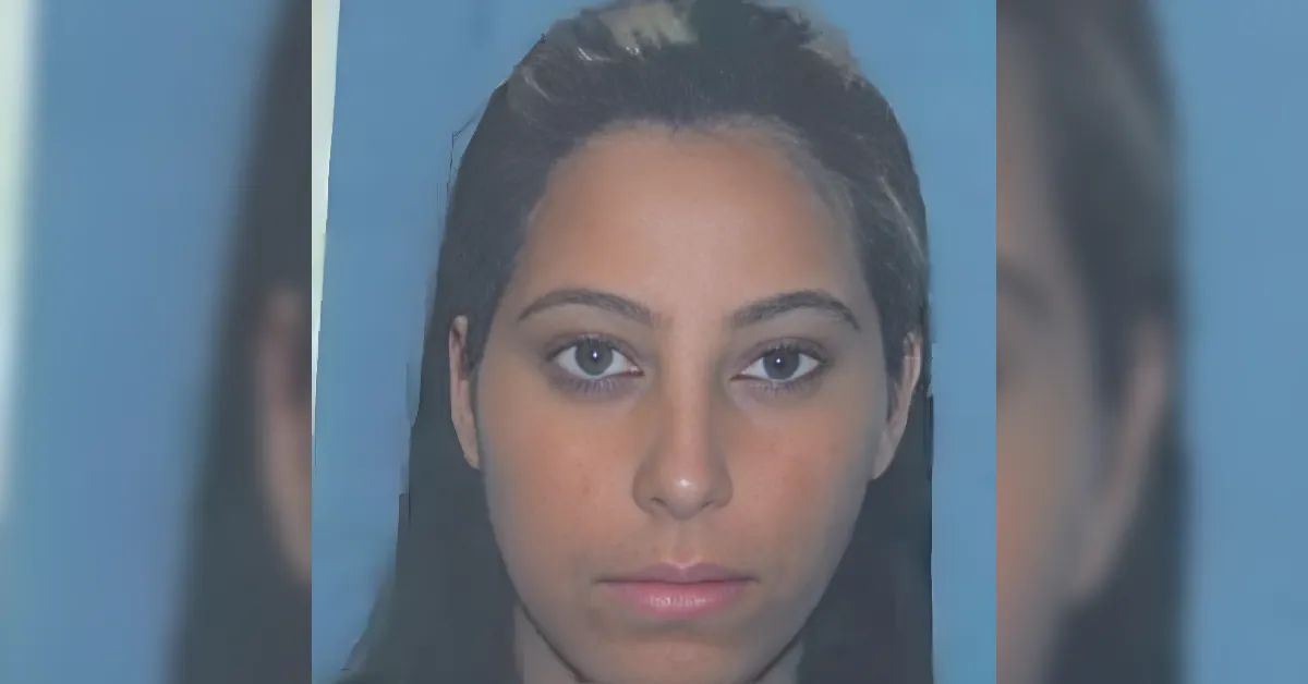 Close-up portrait of a young woman with dark hair against a blue background, neutral expression.