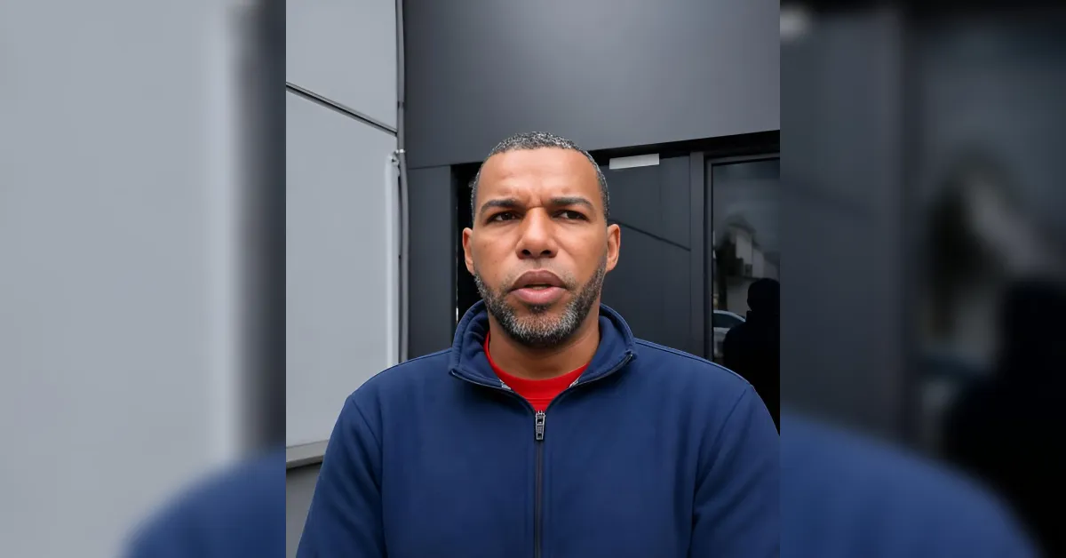 Man with short hair and beard wearing a blue zip-up jacket outside a modern building.
