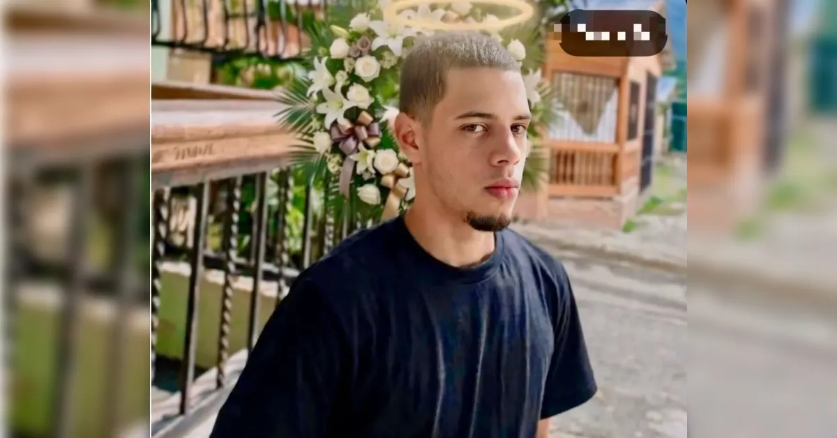 Young man with bleached blond hair and a goatee in a black t-shirt, standing outdoors with floral arrangements in the background.