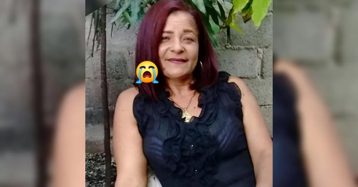 Smiling woman with shoulder-length red hair in a black ruffled blouse sits outdoors against a brick wall; there is a crying emoji over her left side.