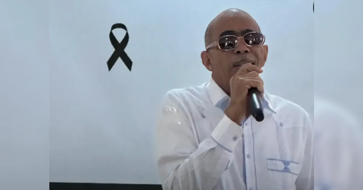 Man in a white shirt with sunglasses singing into a handheld microphone on stage.