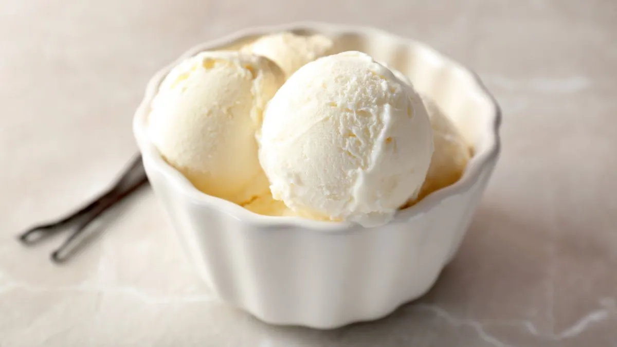 Two scoops of vanilla ice cream in a white fluted ramekin on a light marble surface