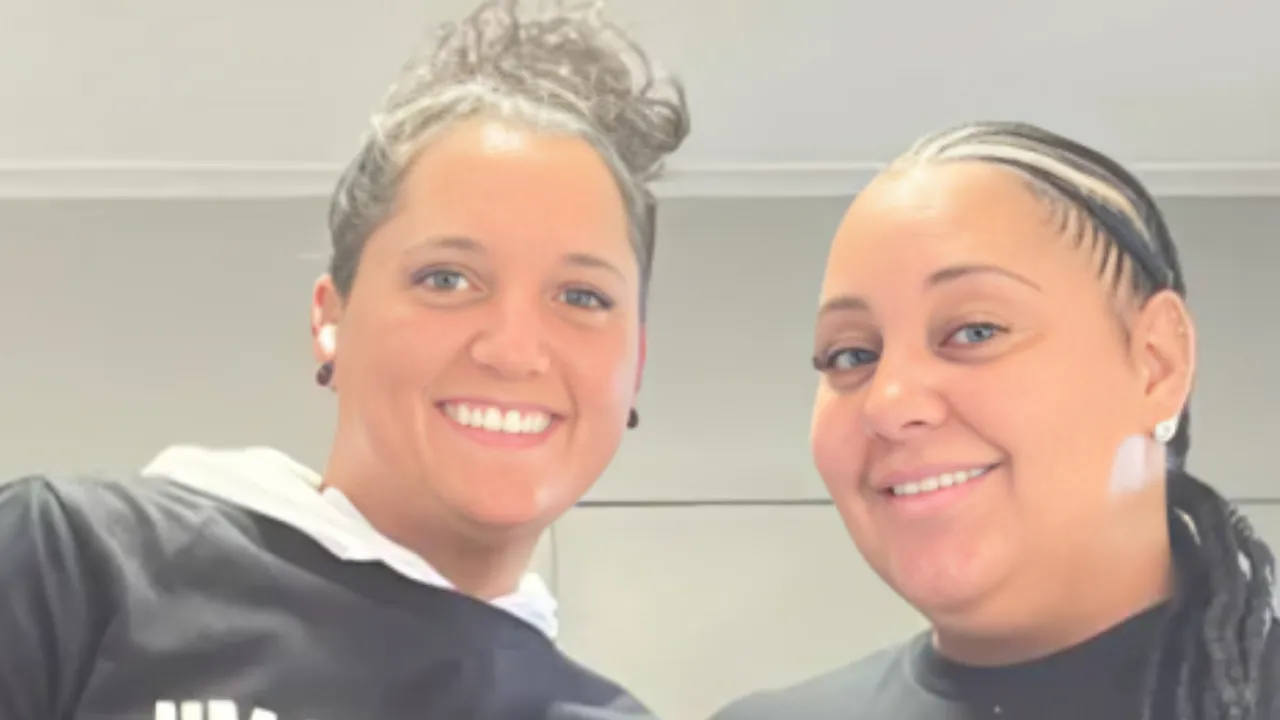 Two women smiling at the camera while posing for a selfie indoors.