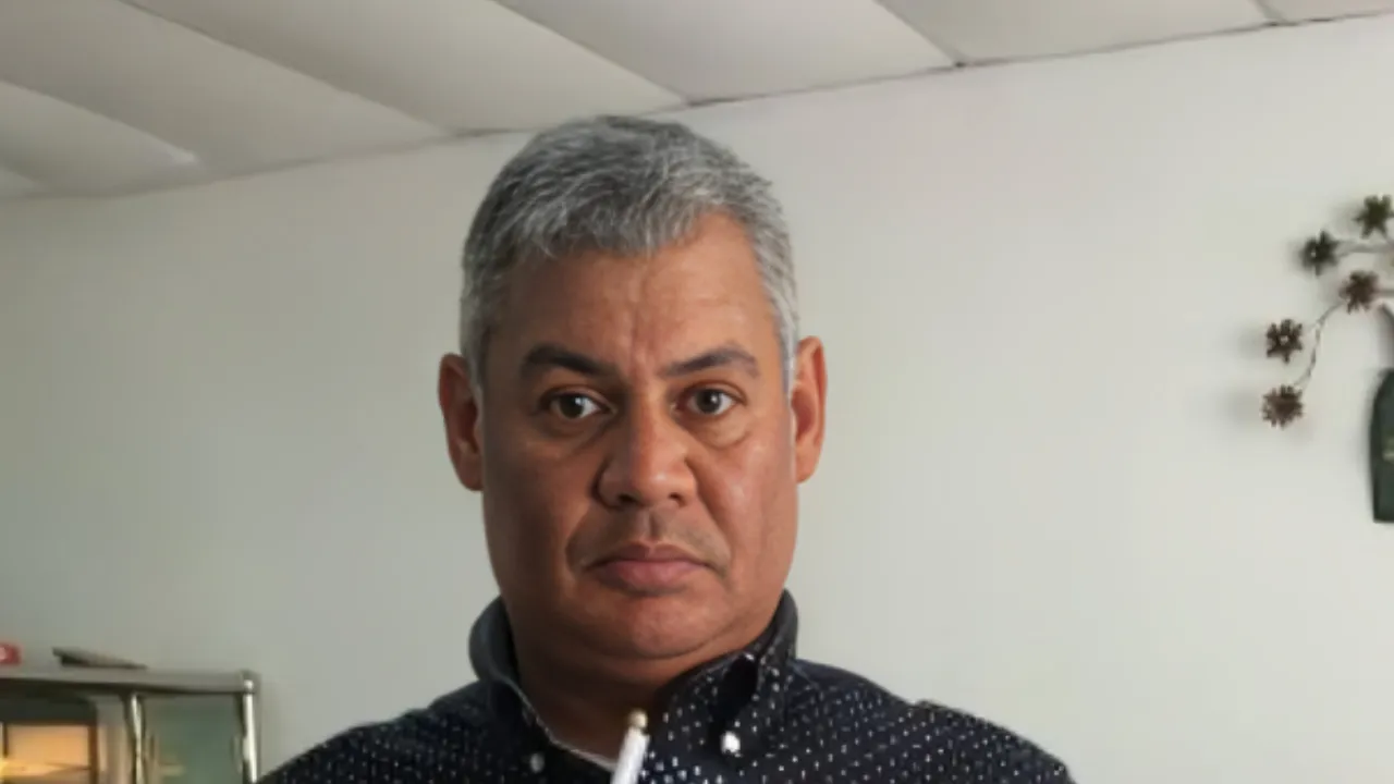 A middle-aged man with short gray hair wearing a dark polka-dot shirt, looking straight at the camera in a neutral indoor setting.