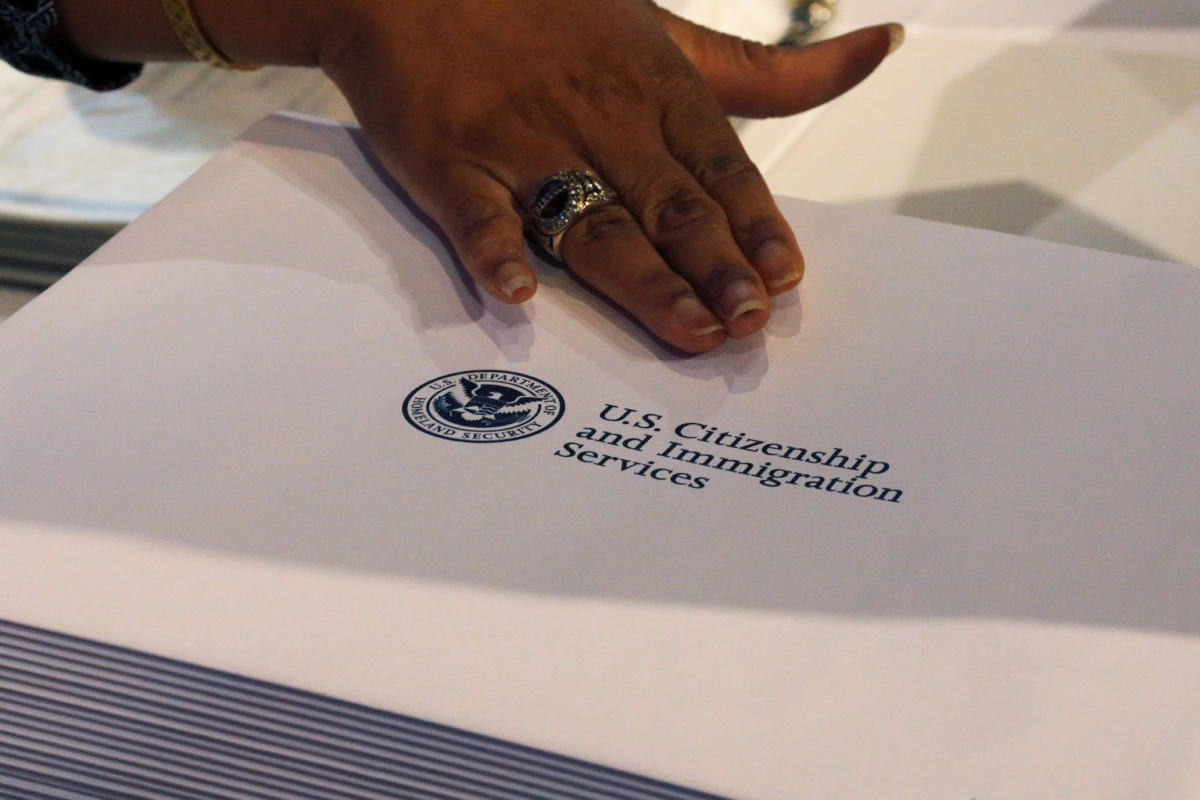 Close-up of a hand resting on a U.S. Citizenship and Immigration Services document with the agency seal visible on the page.