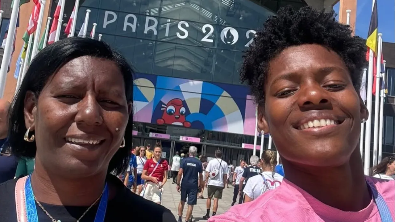 Two women smiling for a selfie outside a modern venue with flags and a colorful mural in the background.