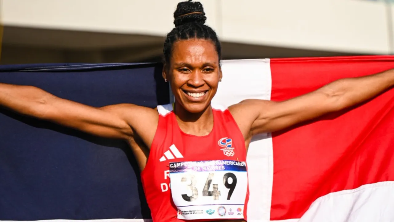 Female athlete proudly holding a Dominican Republic flag with arms outstretched, wearing a red race kit and bib 349, smiling at the finish or celebration moment.