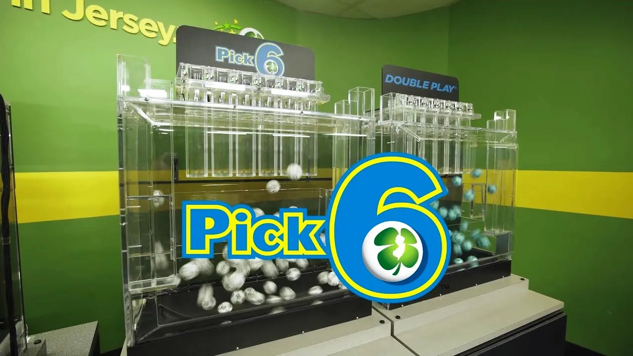 Clear acrylic lottery-style ball machine displaying white balls labeled 'Pick 6' with a large blue and yellow '6' logo and green walls in the background, suggesting a lottery game setup.