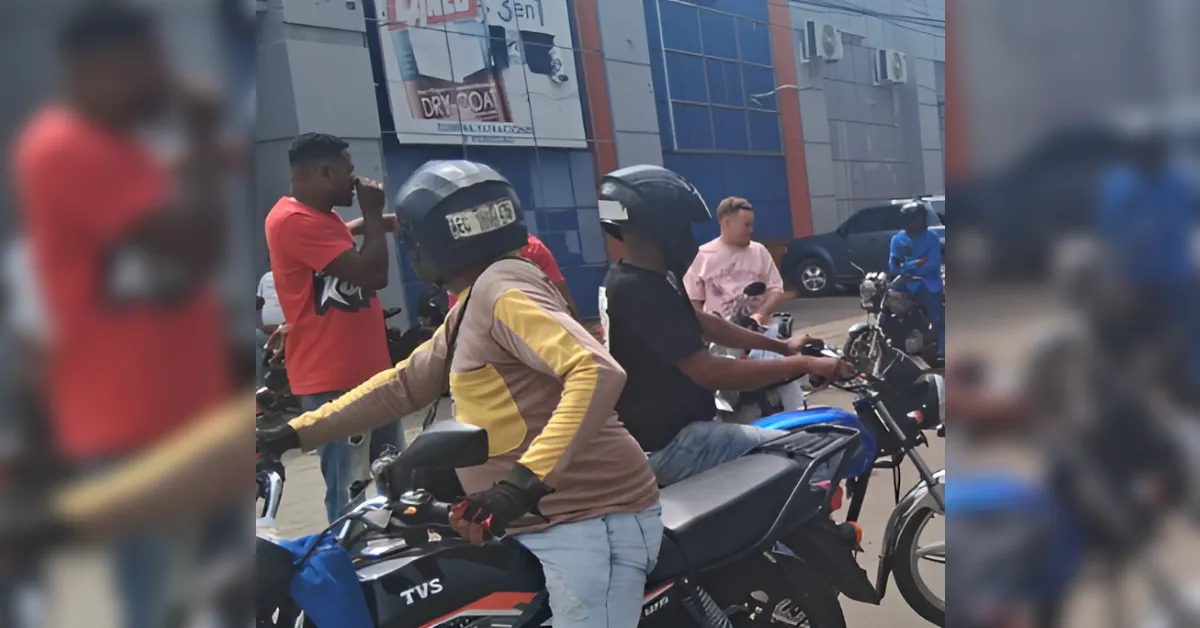 Riders wearing helmets on motorcycles in a parking lot by a blue storefront building.