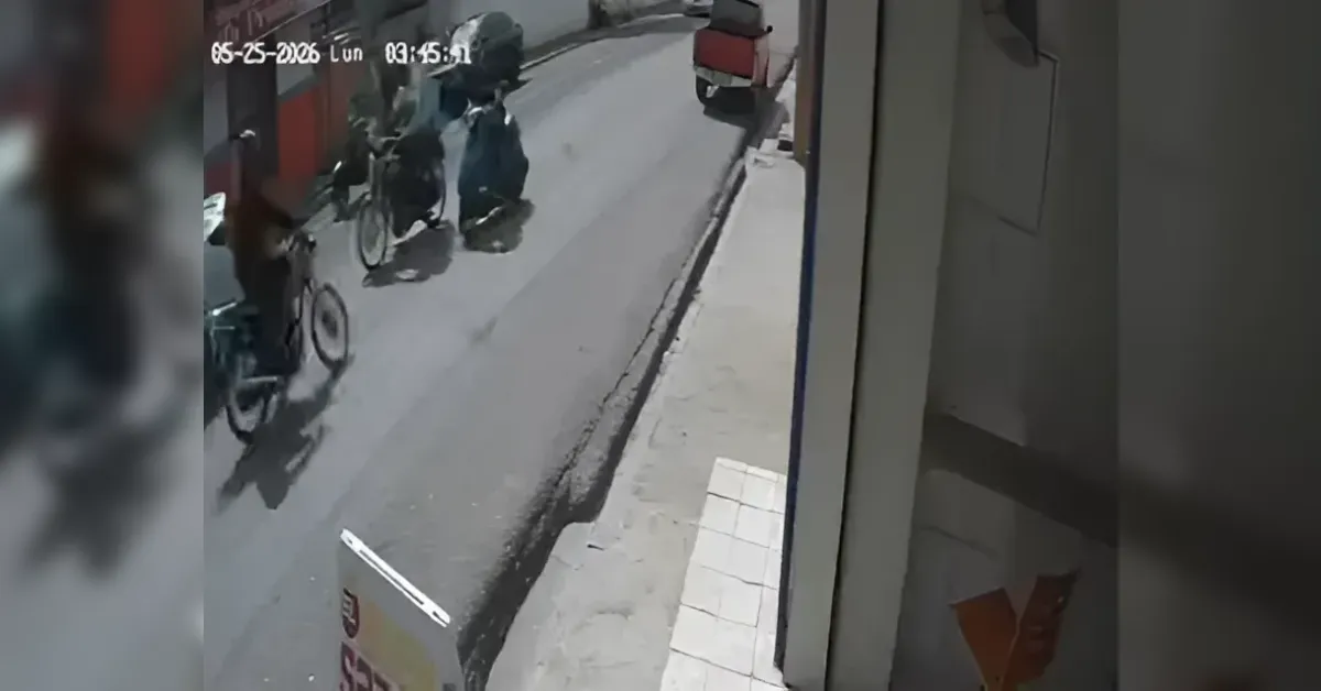CCTV footage of a narrow street with bicycles parked along the curb and pedestrians near a shop entrance.