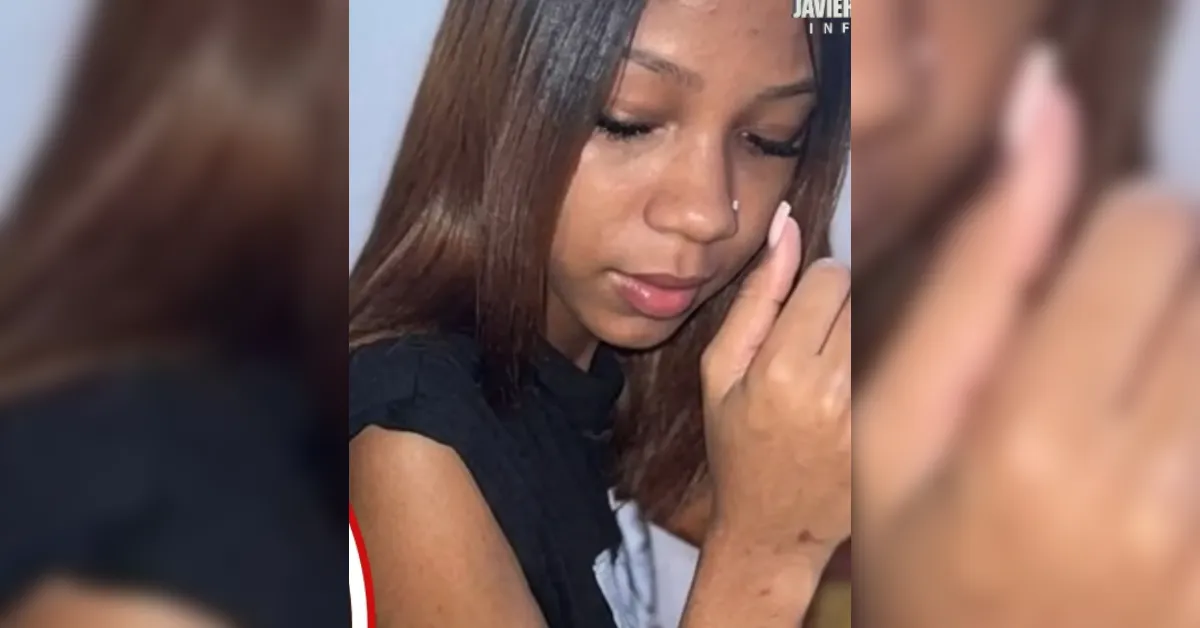 Close-up of a young woman with straight brown hair looking down, touching her face with a finger near her cheek.