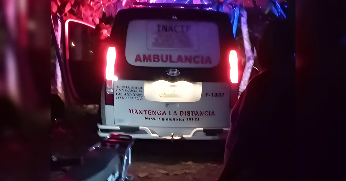Rear of an ambulance at night with red taillights on, displaying 'AMBULANCIA' and 'MANTENGA LA DISTANCIA' on the bumper sign.