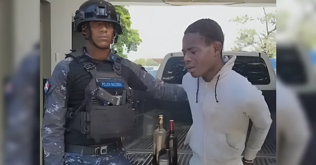 Uniformed soldier in tactical gear and helmet stands beside a young man in a light hoodie near a pickup truck, bottles resting on the tailgate.