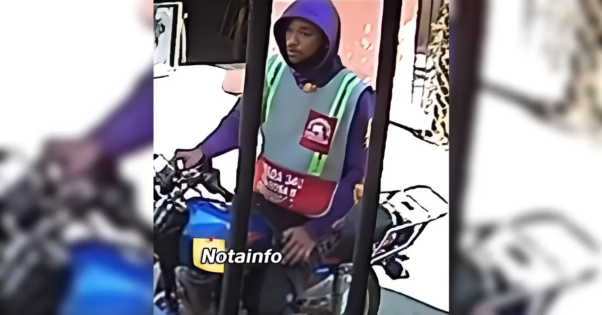 Person wearing a purple hijab and a reflective safety vest sits on a blue motorcycle at a gas station.
