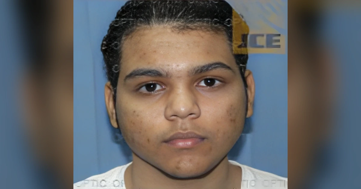Frontal mugshot photo of a young man with facial acne against a blue backdrop.