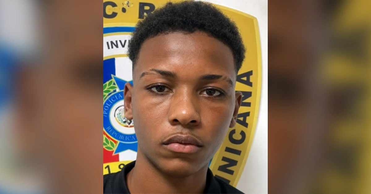 Young man facing the camera with a police emblem behind him, in a close-up portrait style.