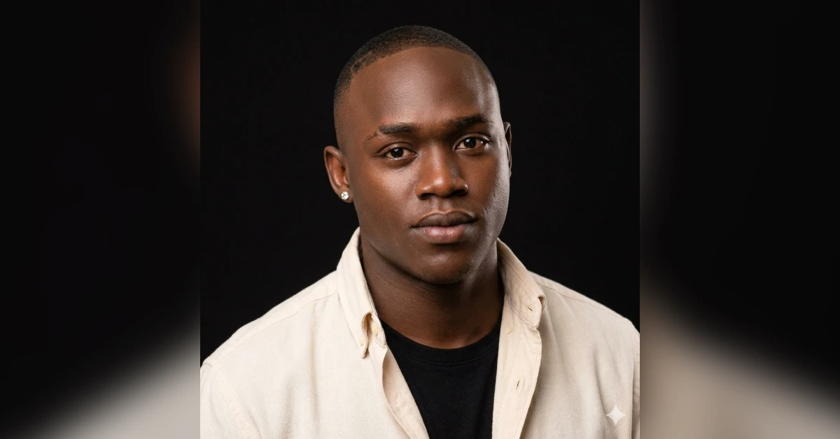 Portrait of a young Black man with short hair, wearing a beige shirt over a black tee, against a dark studio background.