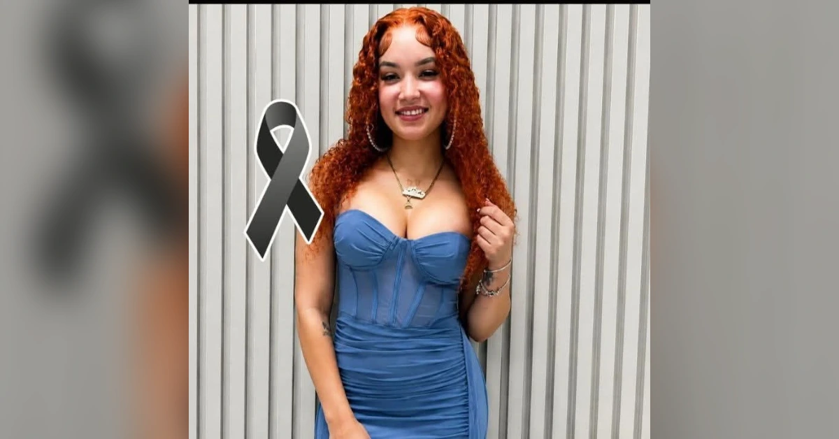 Woman with red curly hair in a blue strapless dress stands against a striped wall, with a black awareness ribbon overlay.
