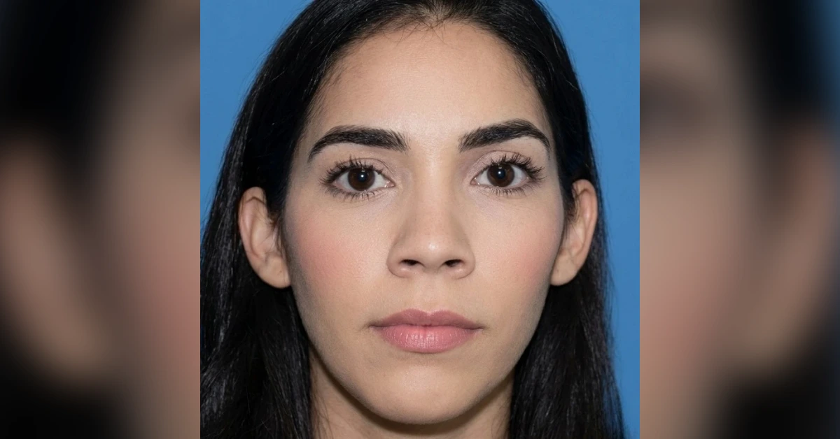 Close-up portrait of a young woman with dark hair and brown eyes against a blue background, looking at the camera with a neutral expression.