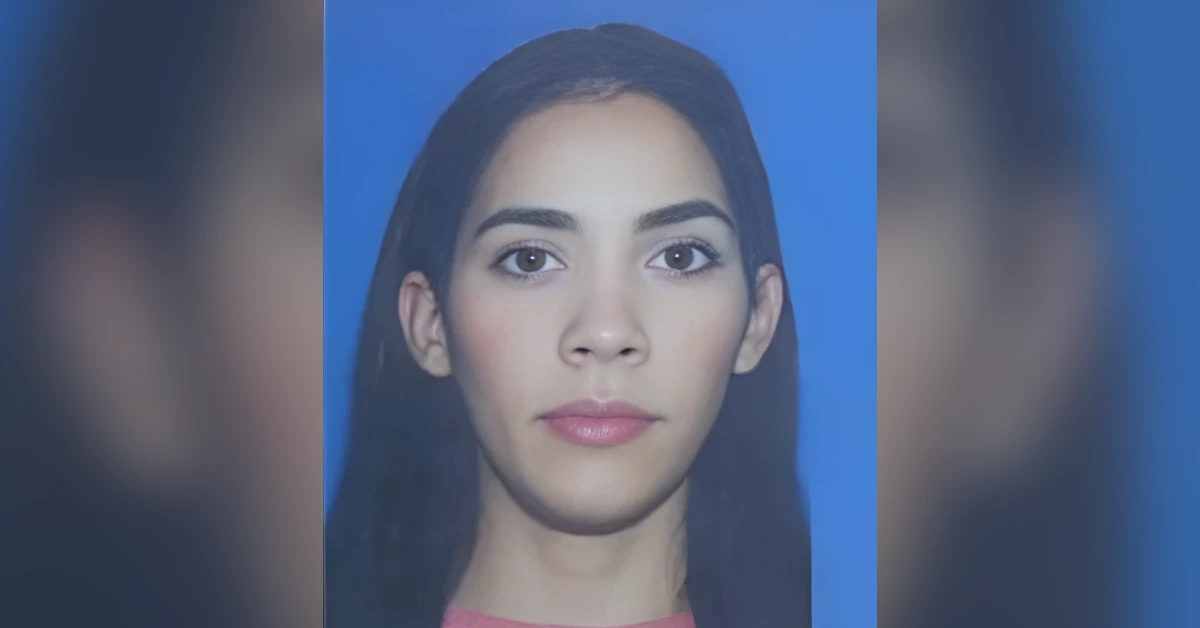Portrait of a young woman with long dark hair against a blue background, neutral expression, suitable for ID photo