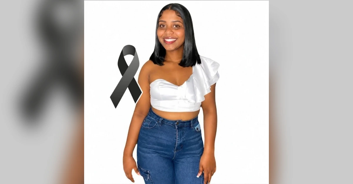 Smiling woman in a white one-shoulder top and blue jeans standing beside a black awareness ribbon on a white background.