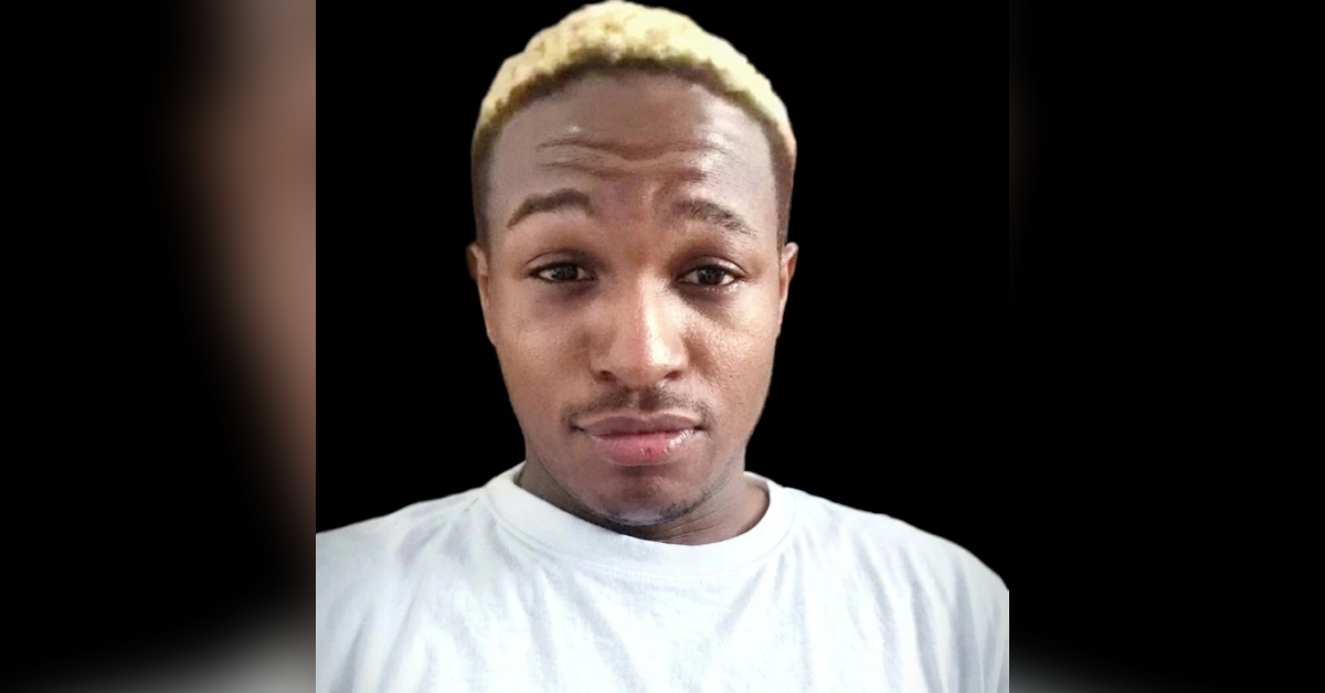 Portrait of a young man with bleached blond hair wearing a white T-shirt, against a black background, looking at the camera with a neutral expression.
