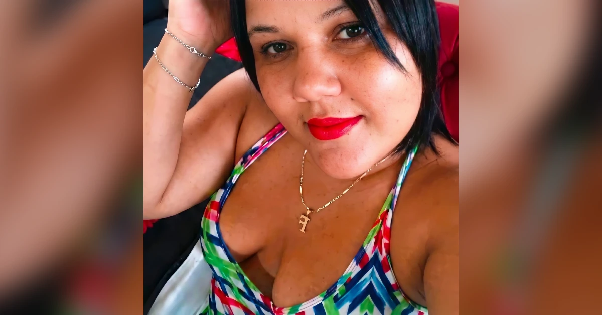 Close-up selfie of a woman with red lipstick wearing a colorful patterned bikini top and a gold necklace.