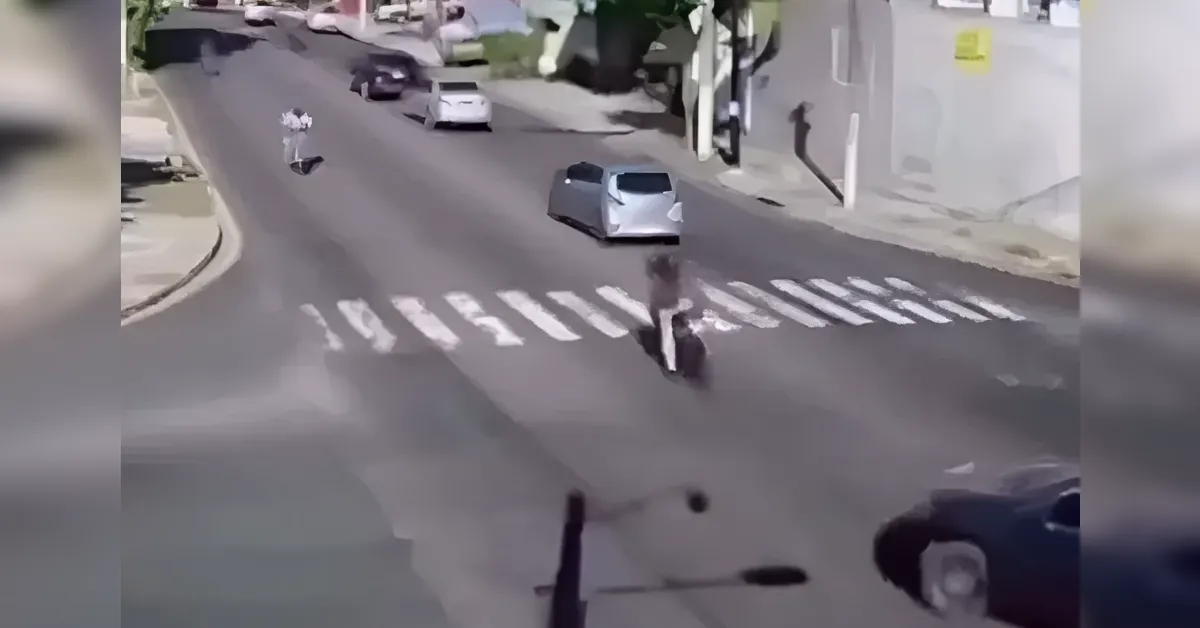 Person riding a scooter across a zebra crosswalk at a city intersection, with cars and buildings in view.