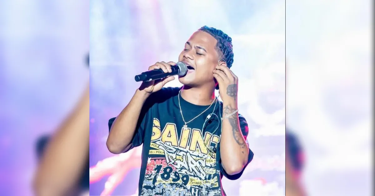 Male singer performs on stage, singing into a microphone with eyes closed, wearing a graphic T-shirt and headphones.
