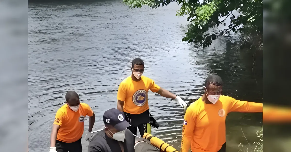 Rescue team in orange shirts by a river, wearing masks and gloves, preparing a yellow inflatable raft.