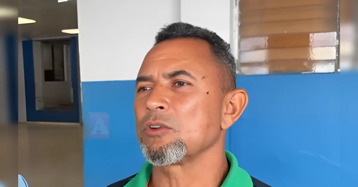 Close-up of a man with a gray goatee speaking, indoors against a blue wall (interview style).
