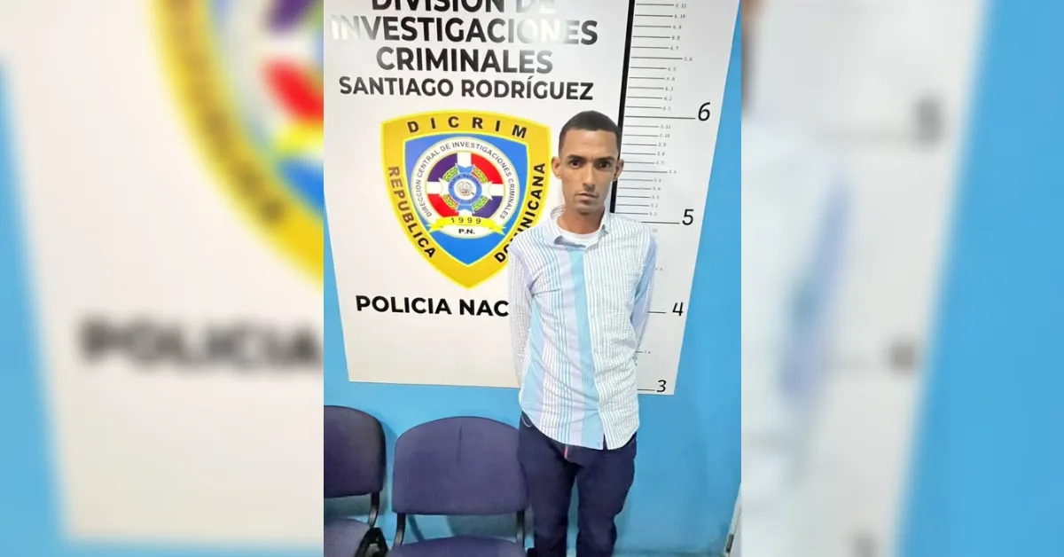 Man standing in a police mugshot setup against a height chart and a police shield, in a blue-walled room.