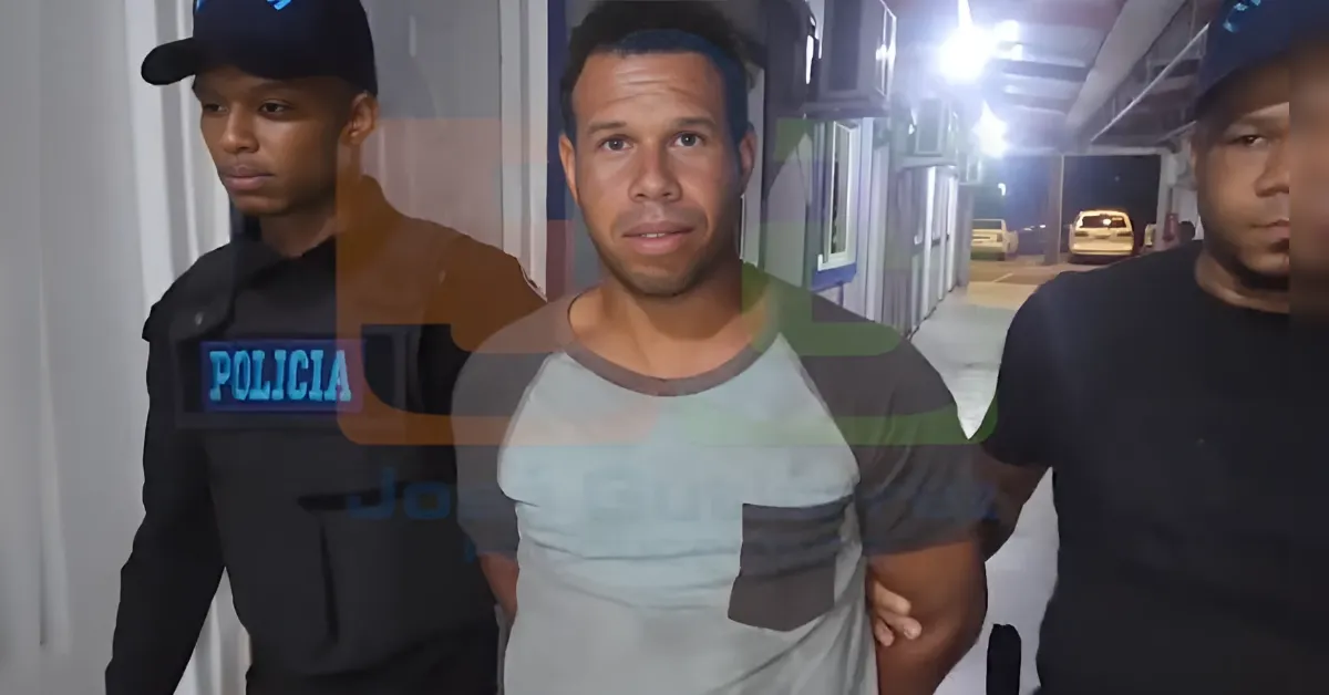 Two police officers escort a man in a gray T-shirt down a dim hallway at night.