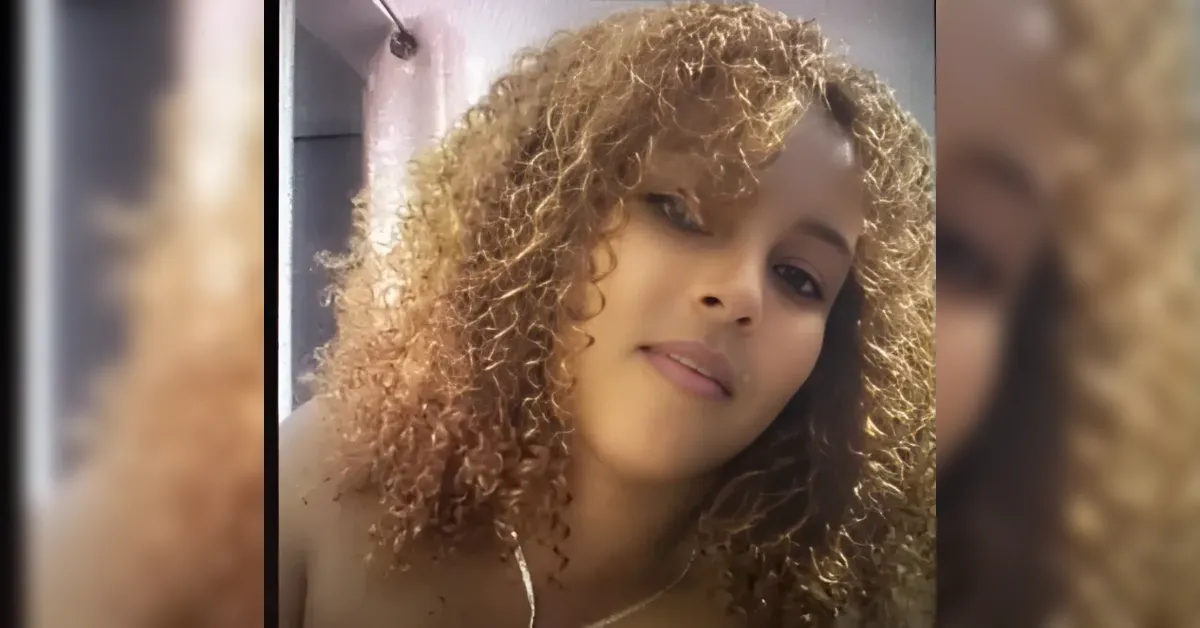 Close-up portrait of a woman with shoulder-length curly brown hair, softly smiling at the camera.