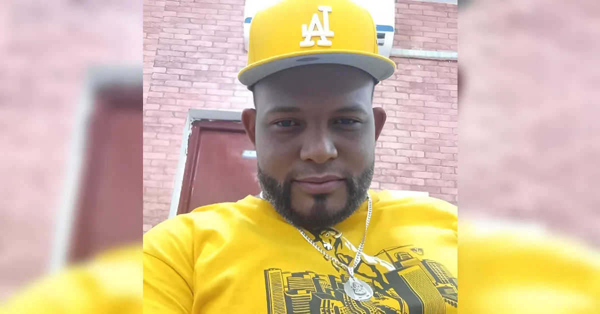 Selfie of a man wearing a yellow LA cap and matching yellow t-shirt outdoors in front of a brick wall with a subtle smile.