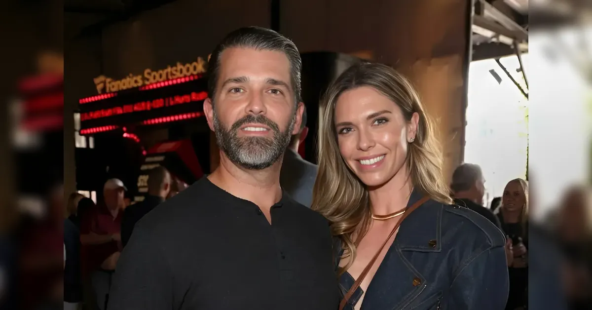 Two smiling adults posing together at a social event; man in a black shirt and woman in a denim jacket stand close to each other in a busy venue.