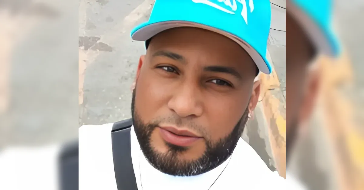 Close-up of a bearded man wearing a bright blue cap and white shirt, looking at the camera outdoors.