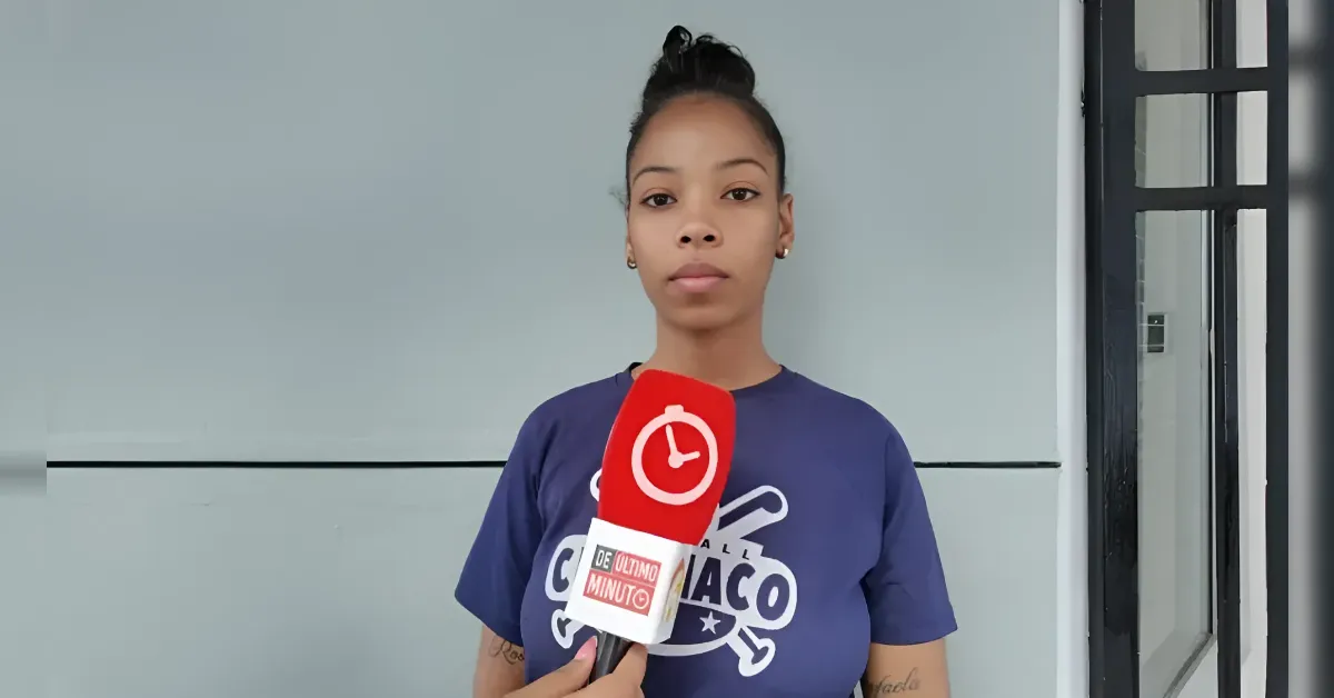 Joven mujer con el cabello recogido sostiene un micrófono rojo de entrevista frente a una pared gris