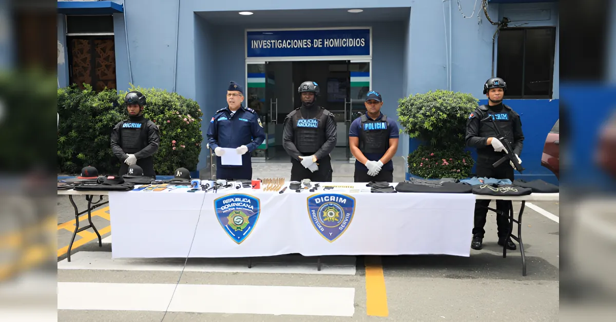 Five officers in tactical gear stand behind a table of seized items outside a homicide investigations building.
