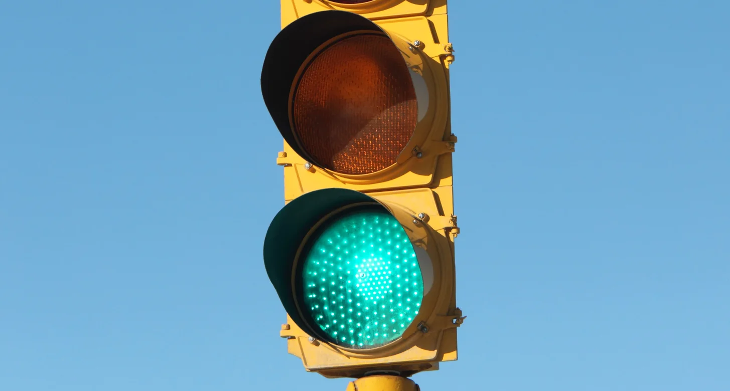 Green traffic light illuminated on a yellow signal housing against a clear blue sky, signaling go.
