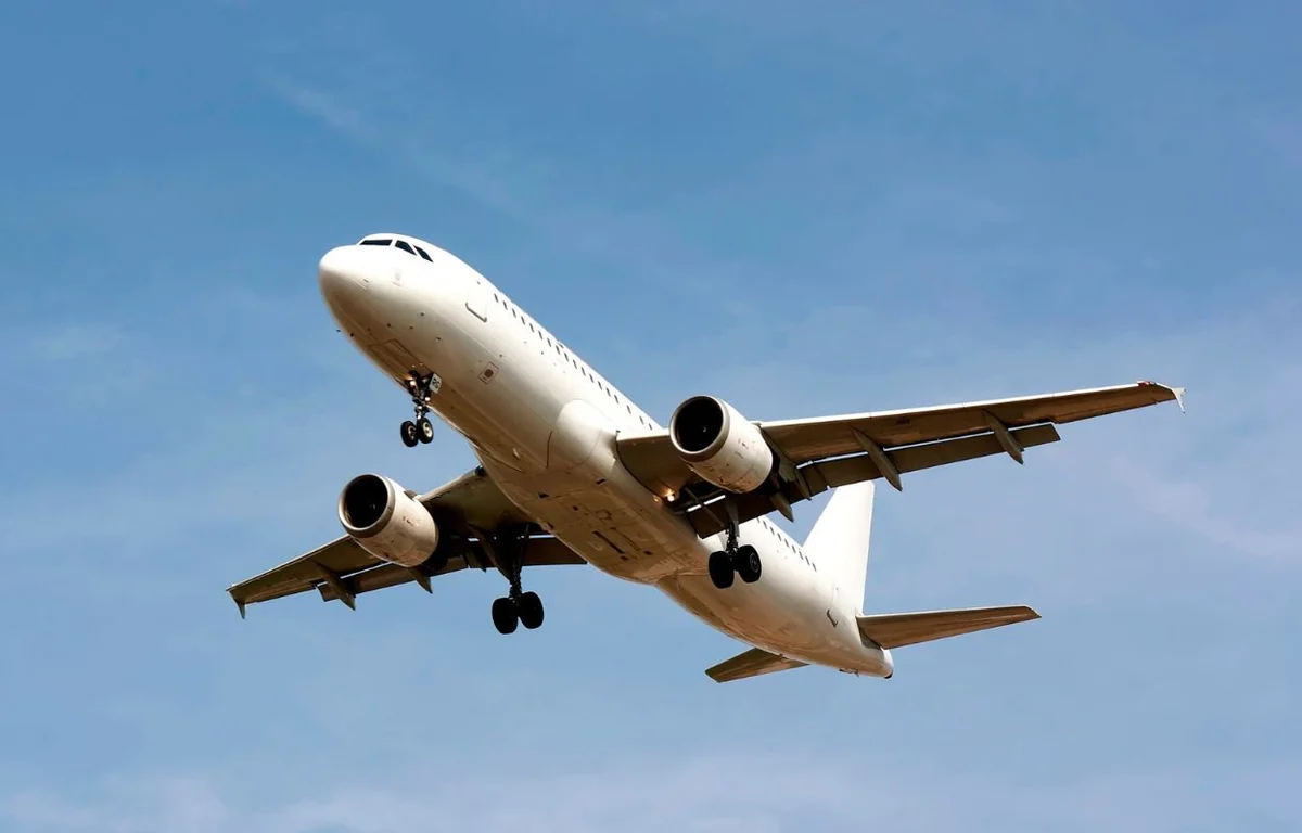 White passenger jet with landing gear down flying against a clear blue sky (mid-flight).