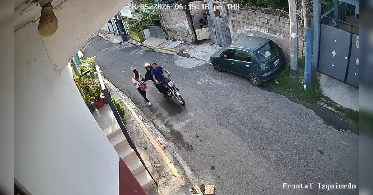 Surveillance image of a narrow street with a parked green car on the right and three people near a motorcycle in the center, viewed from above.