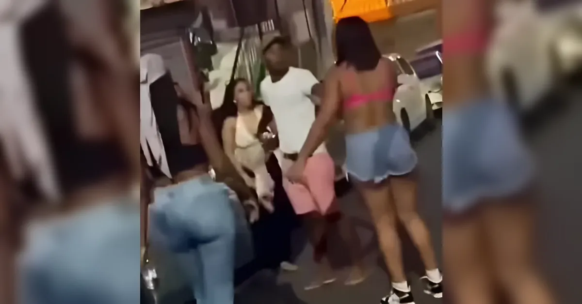 Group of people dancing on a sidewalk at night; woman in pink top and blue shorts foreground, others watching nearby.