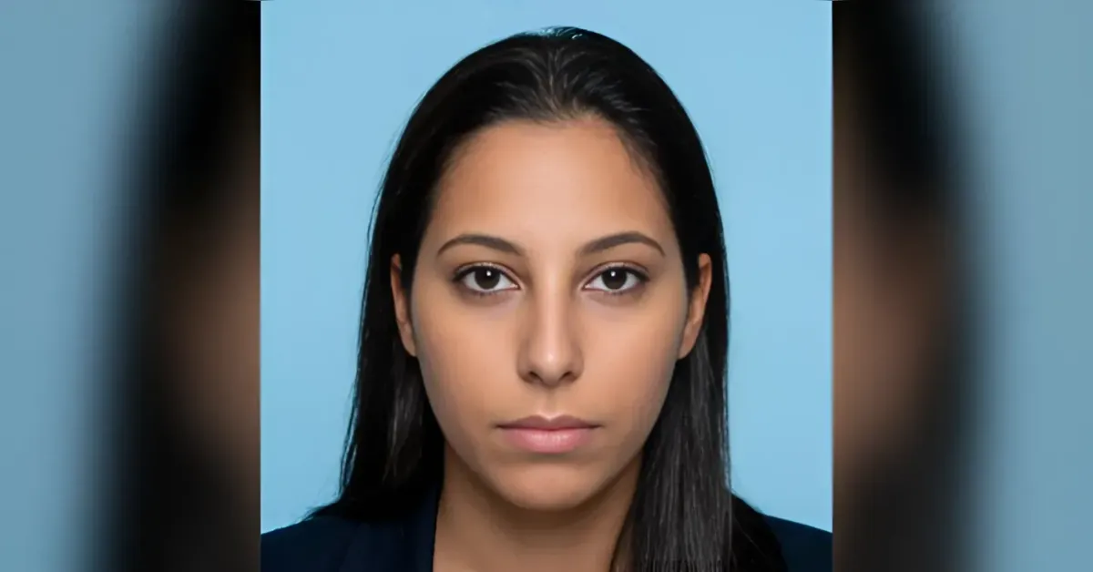 Close-up portrait of a woman with long dark hair and a neutral expression against a light blue background.
