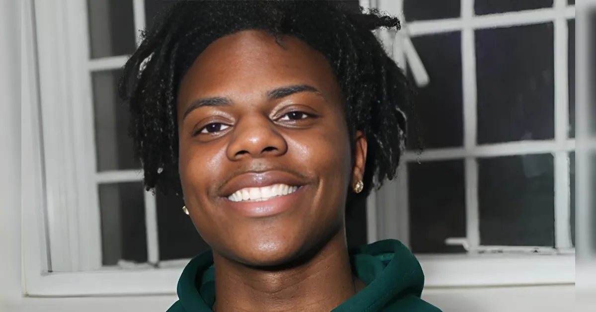Smiling person facing the camera, wearing a dark green hoodie, indoors with a window behind.