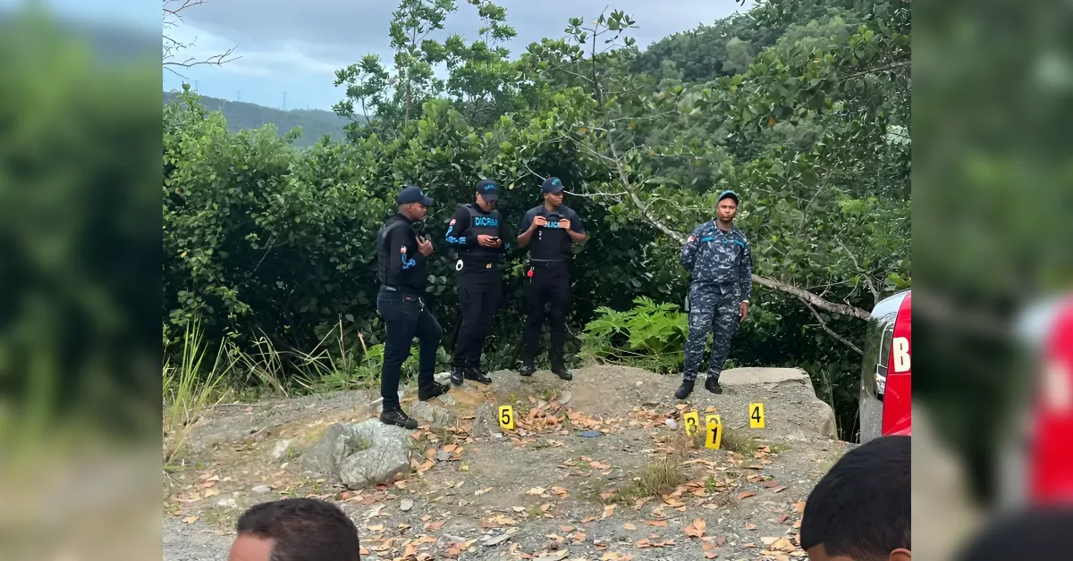 Four officers in tactical gear stand on a rocky ledge with yellow evidence markers (3–5) in front, a red vehicle visible, and dense green brush behind them.